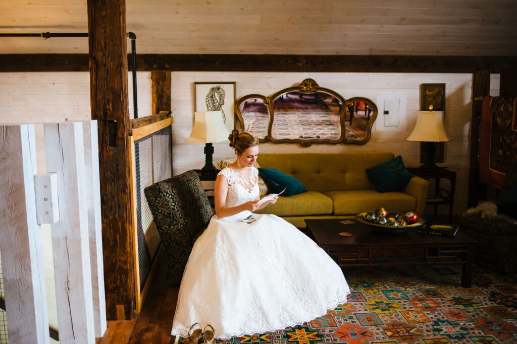 The bride sits on a vintage sofa, reading a heartfelt letter in a warm suite at The Treman Center.