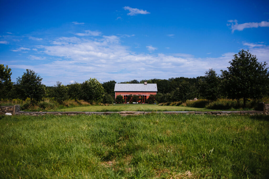 A distant view of The Treman Center’s iconic red barn, surrounded by a green landscape and under a bright blue sky.