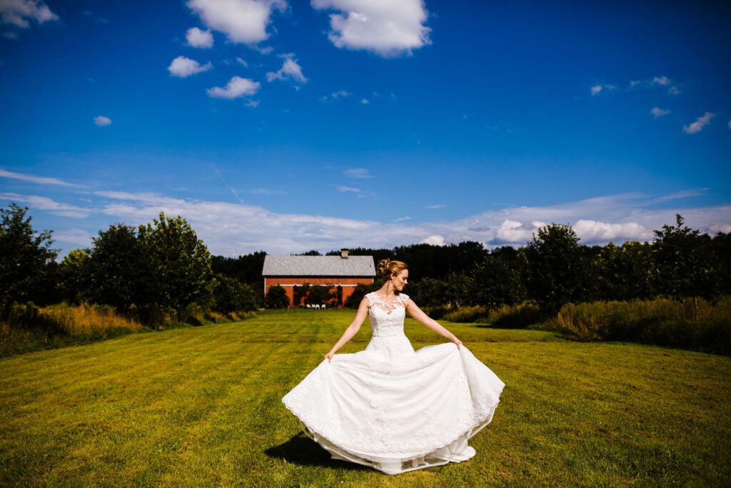 The bride twirls in her flowing white gown on the lawn, with the red barn of The Treman Center as the backdrop.