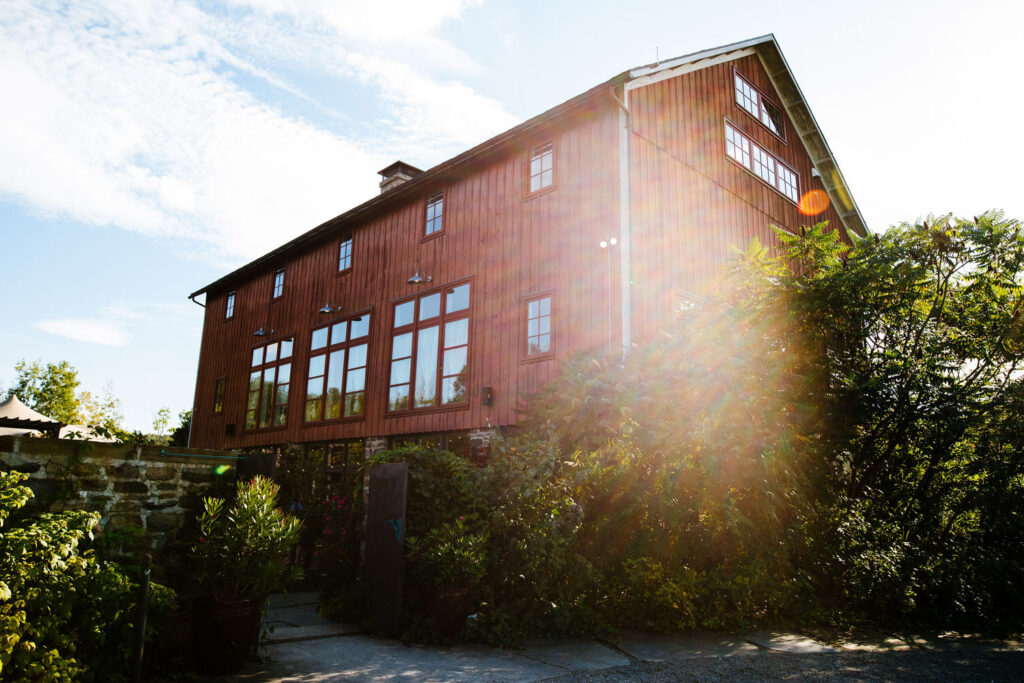 The Treman Center’s red barn exterior, with sunlight streaming through the surrounding trees and plants.