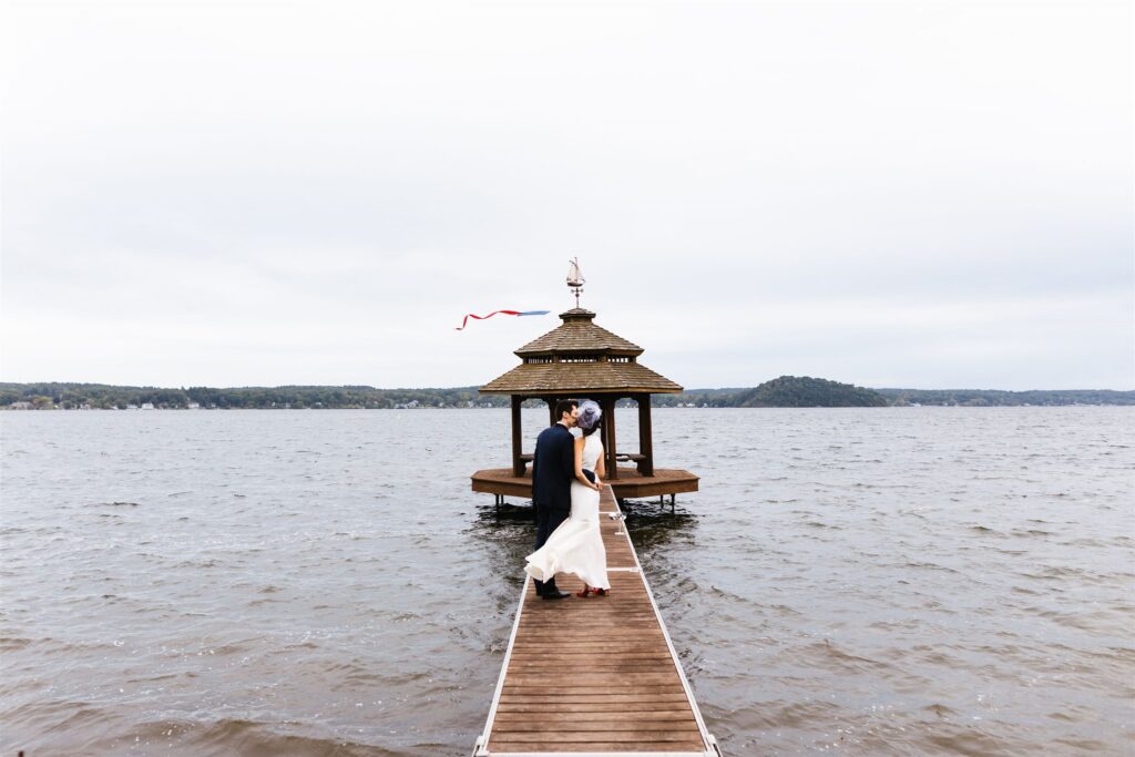 Bride and groom embrace and kiss on a pier in Saratoga Lake in Upstate New York.